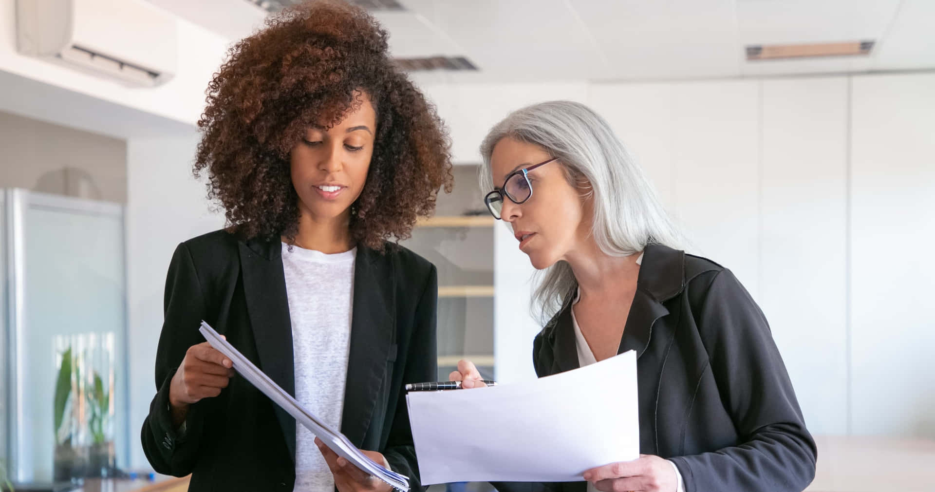 two women in business attire looking at papers