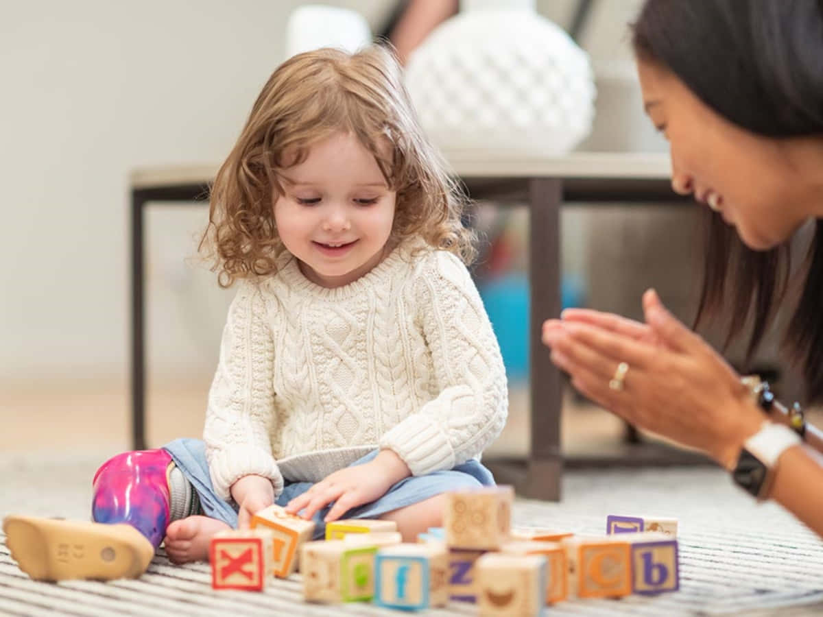 A Young Girl Playing With Wooden Blocks With Her Mother