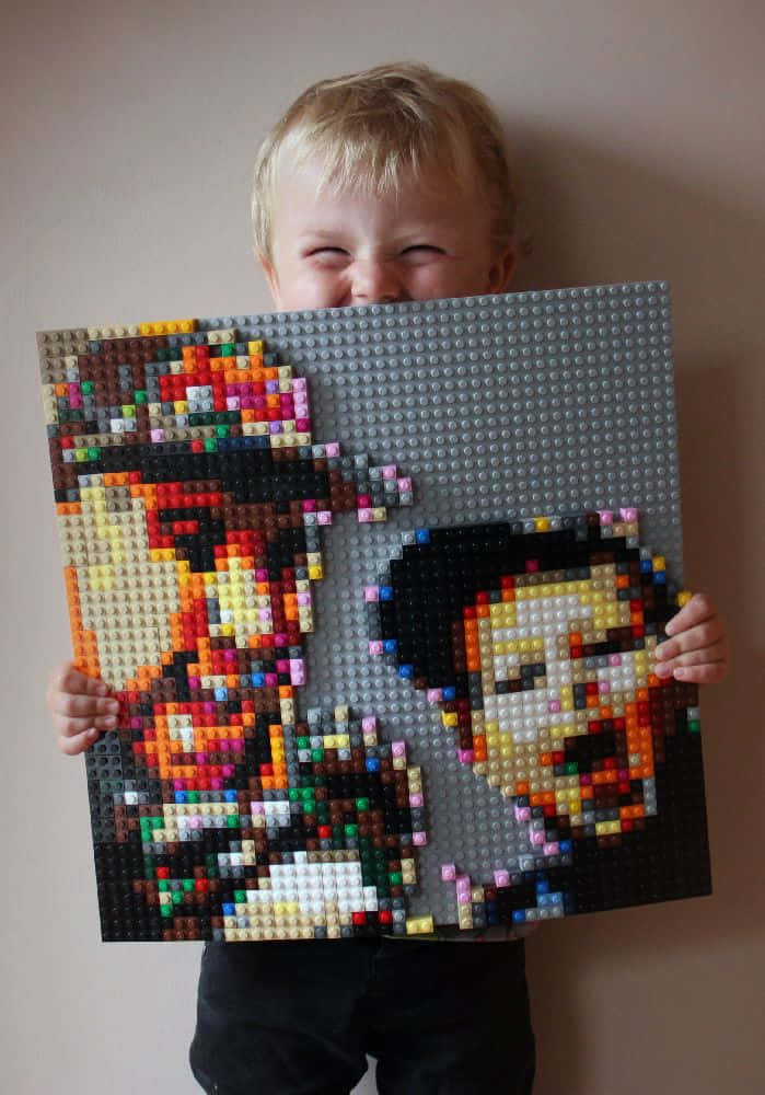 A Young Boy Holding Up A Lego Picture Of Two People