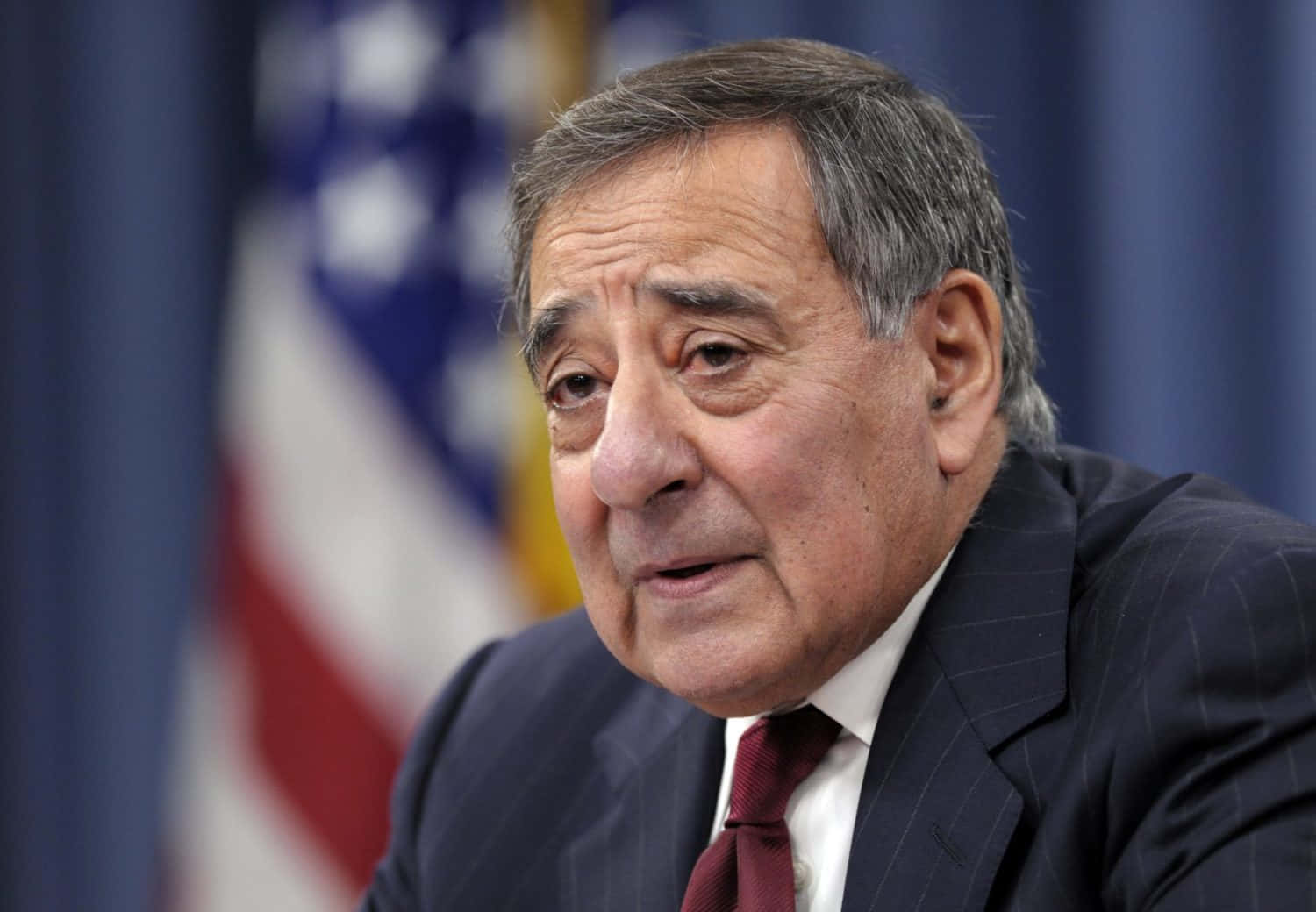 Former Secretary of Defense Leon Panetta stands in front of a blurred American Flag. Wallpaper
