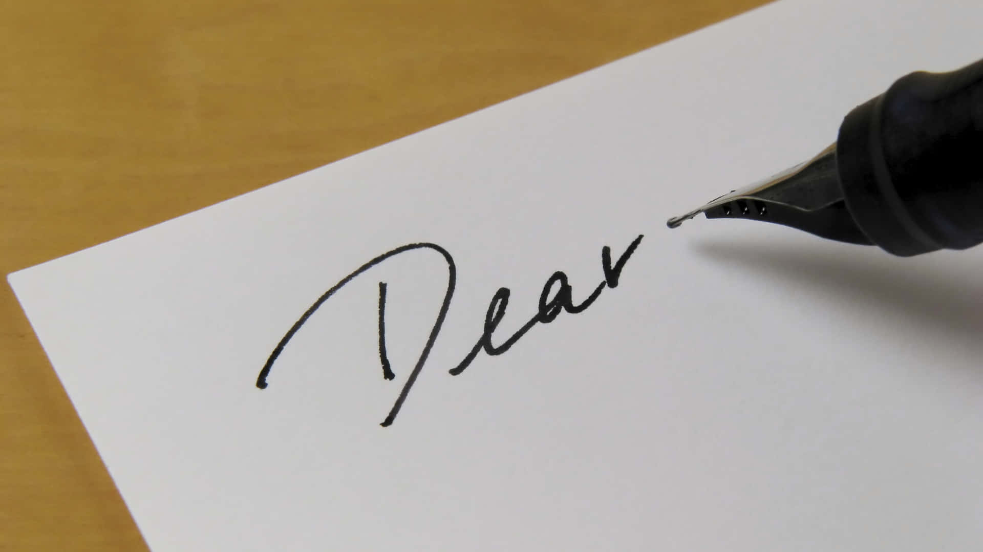 A Pen Is Writing The Word Dear On A Piece Of Paper