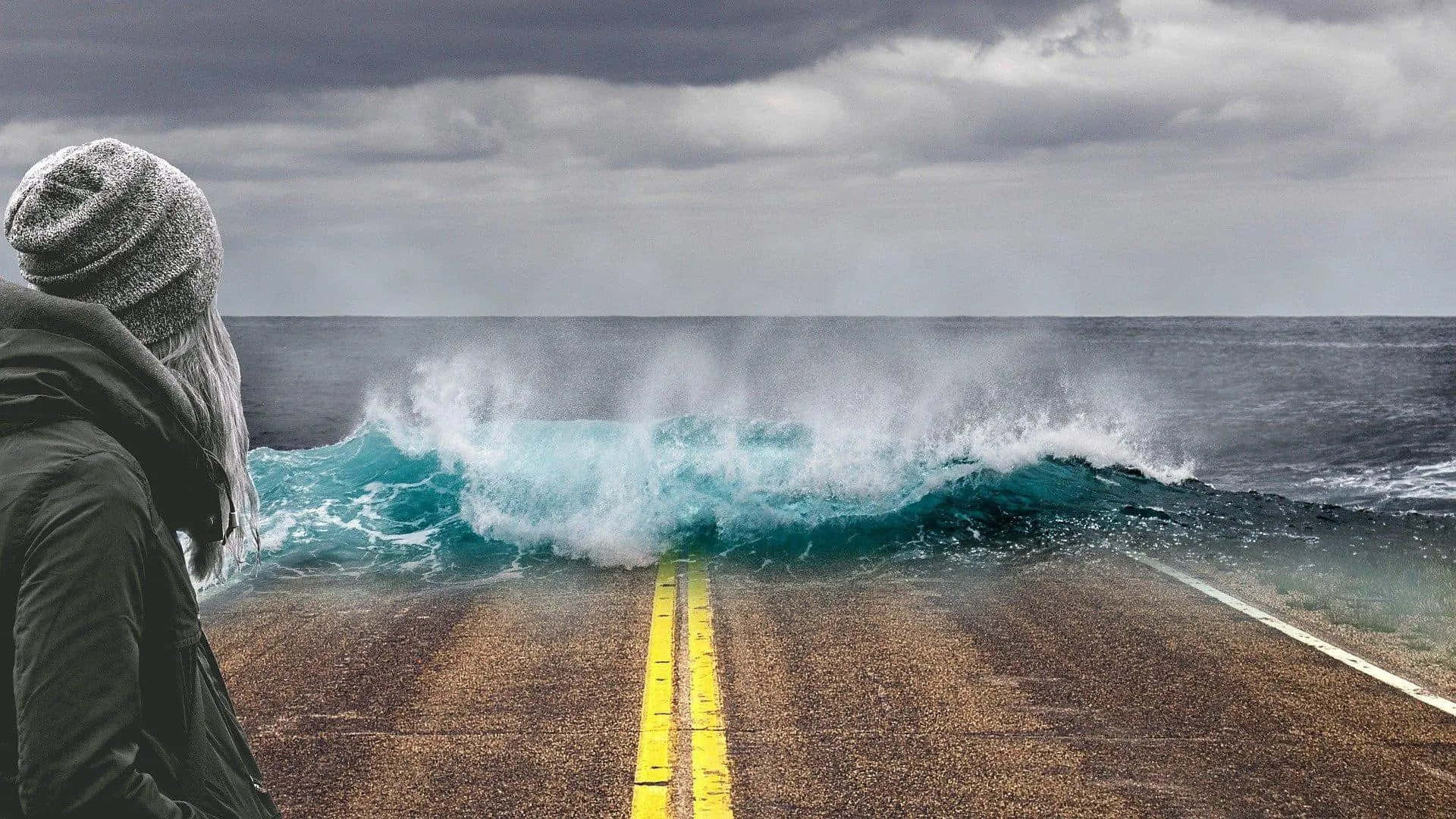 A Person Standing On A Road With Waves Crashing