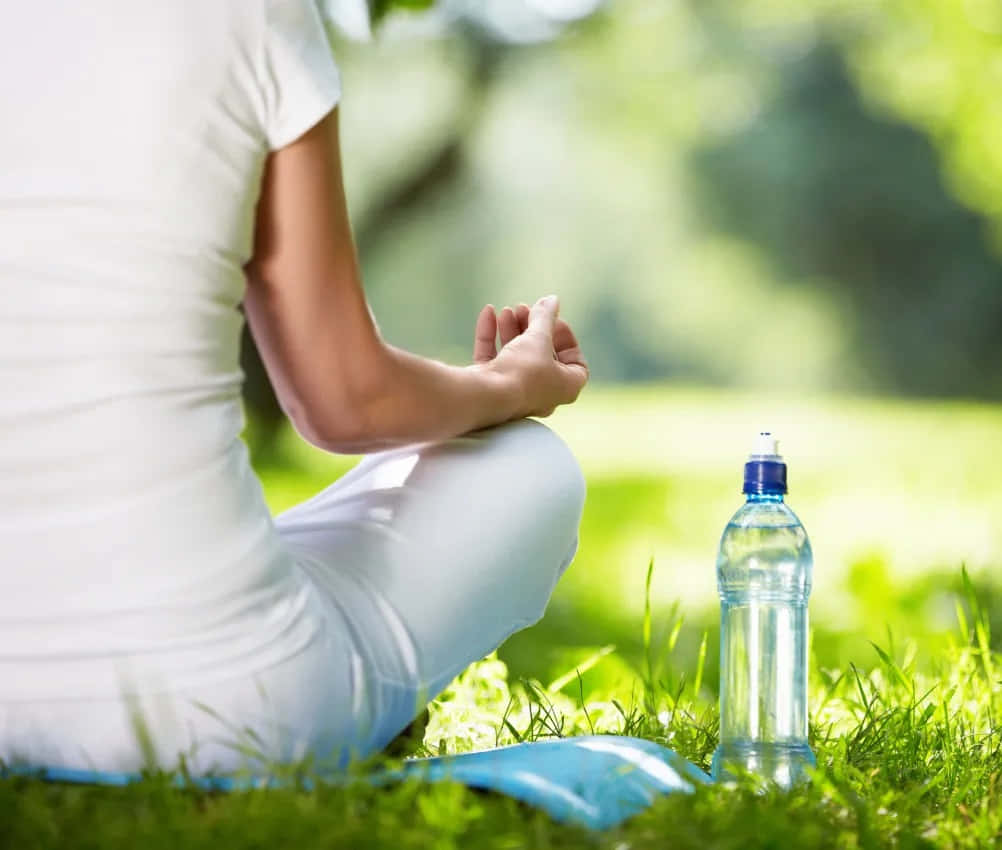 Woman Meditating In The Grass With Water Bottle