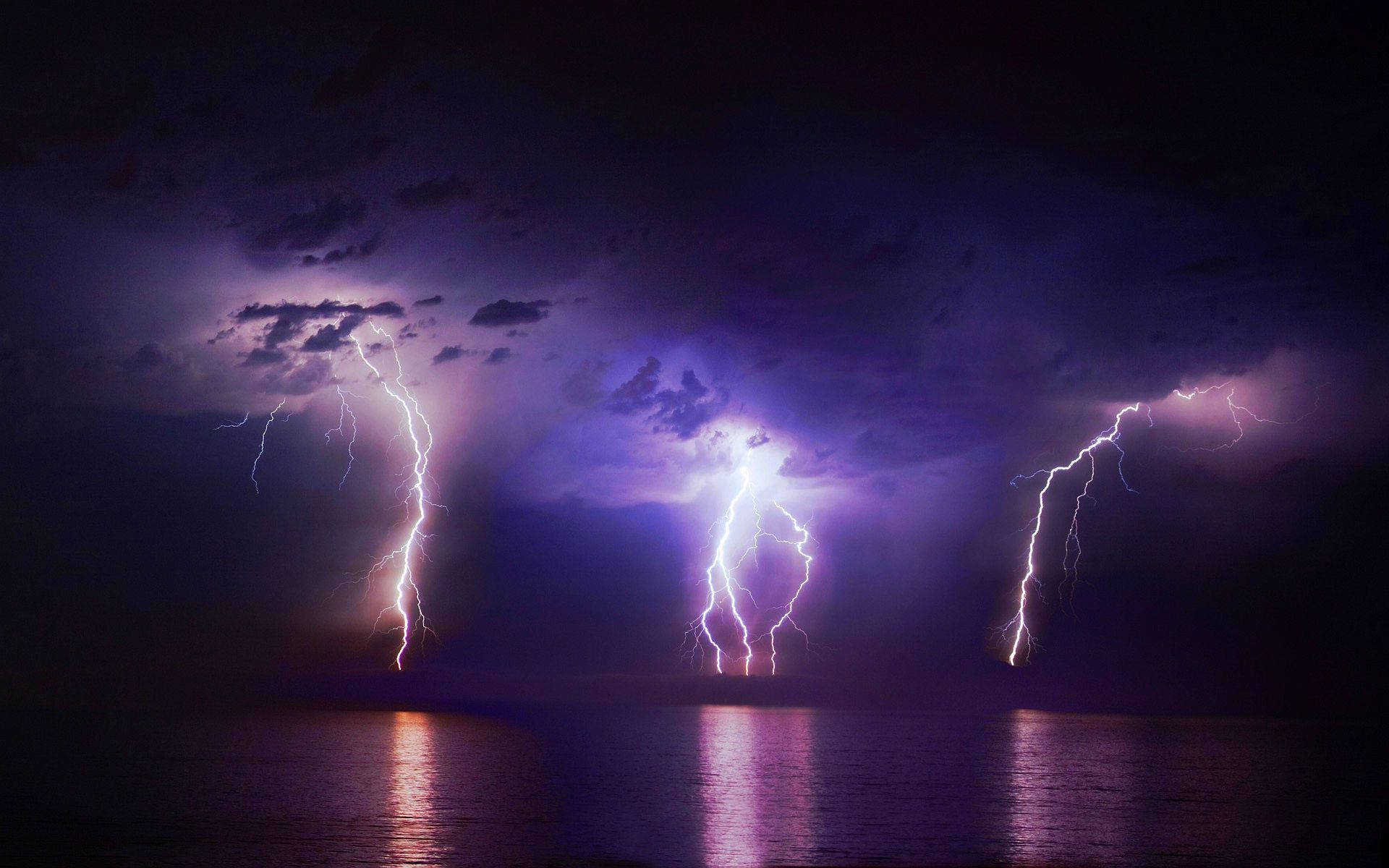 A lightning bolt illuminates the night sky near the ocean. Wallpaper