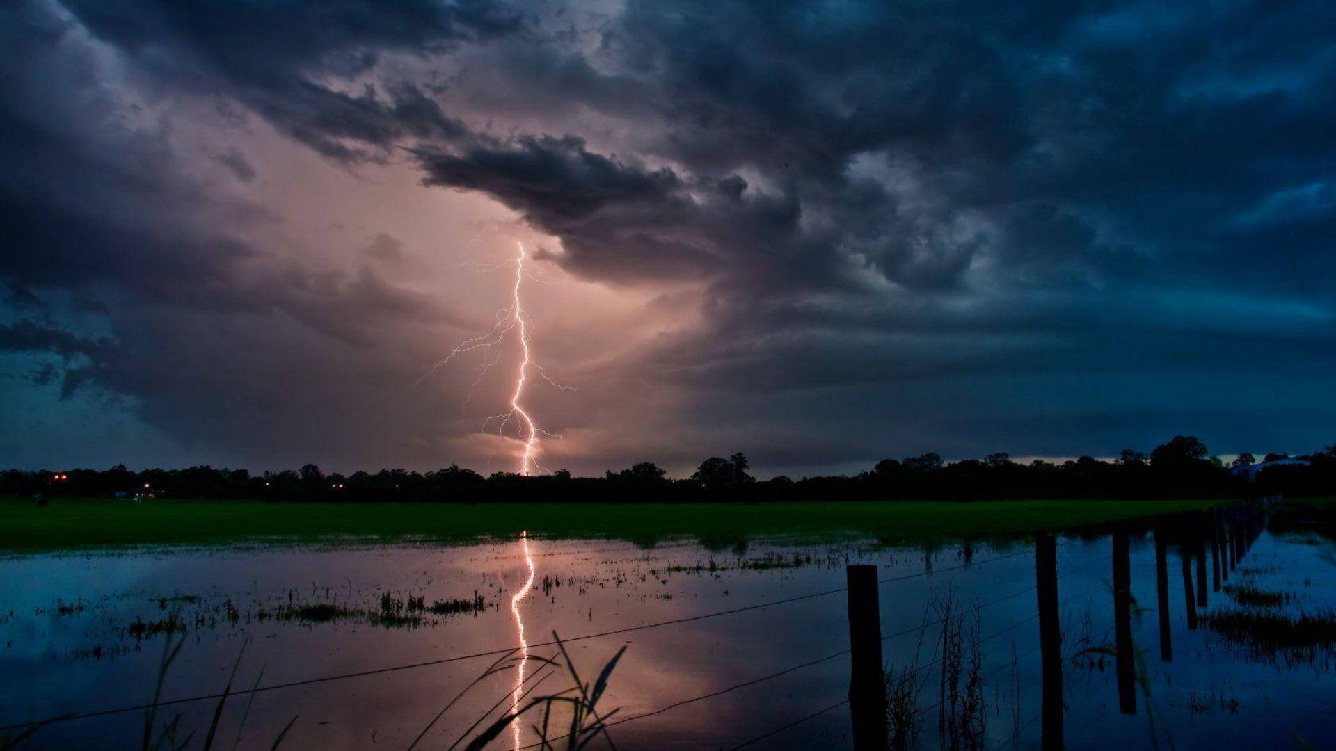 A powerful lightning strike rips through a vast field. Wallpaper