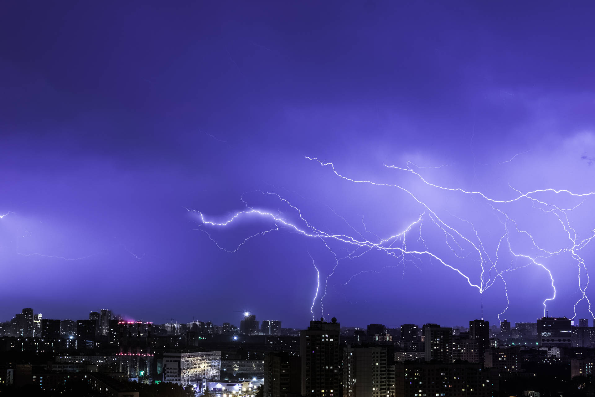 A powerful lightning strike illuminates the night sky of a big city Wallpaper