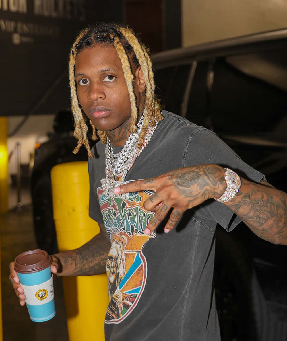 Lil Durk poses in a stylish outfit against a vibrant background