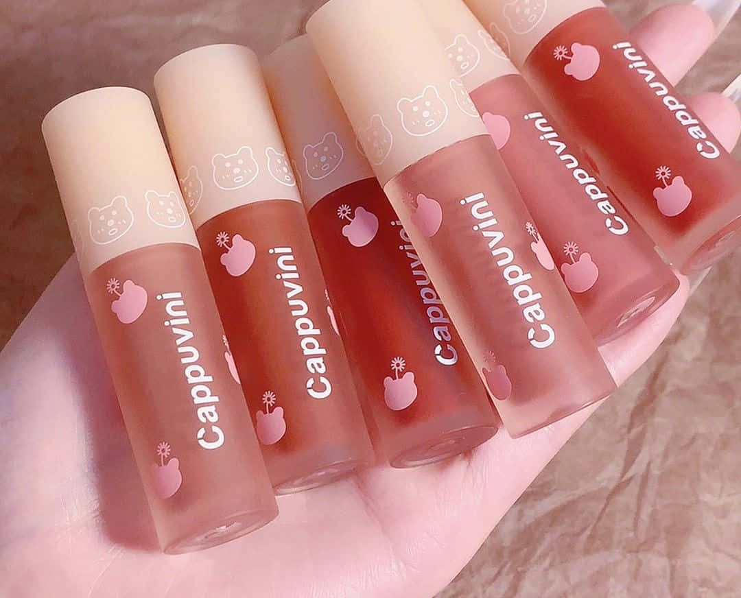 A Hand Holding Five Lip Glosses With Hearts On Them