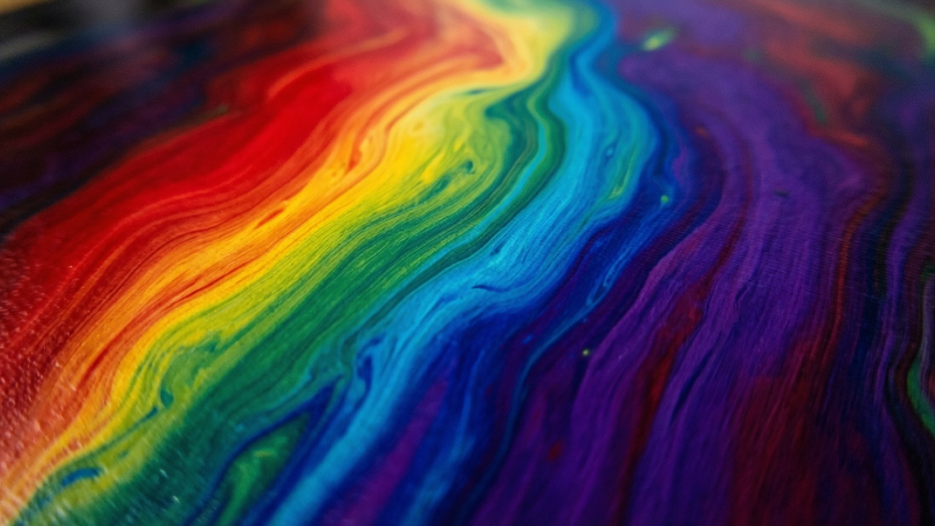 Vivid rainbow colors swirl in fluid motion across a glossy surface.
