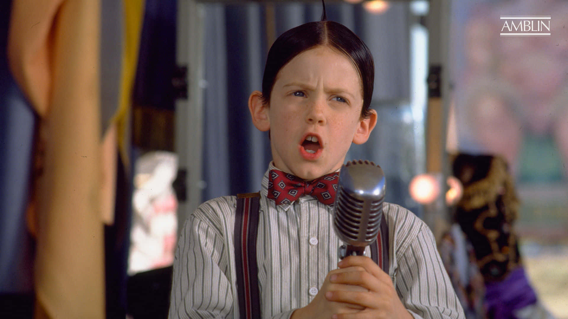 A Boy In A Suspenders Holding A Microphone