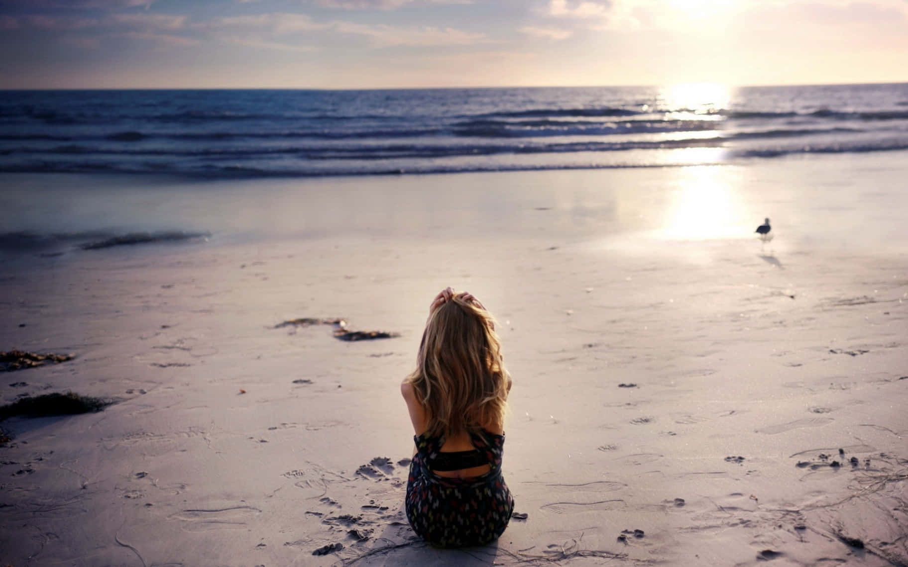 A Woman Sitting On The Beach Looking At The Ocean