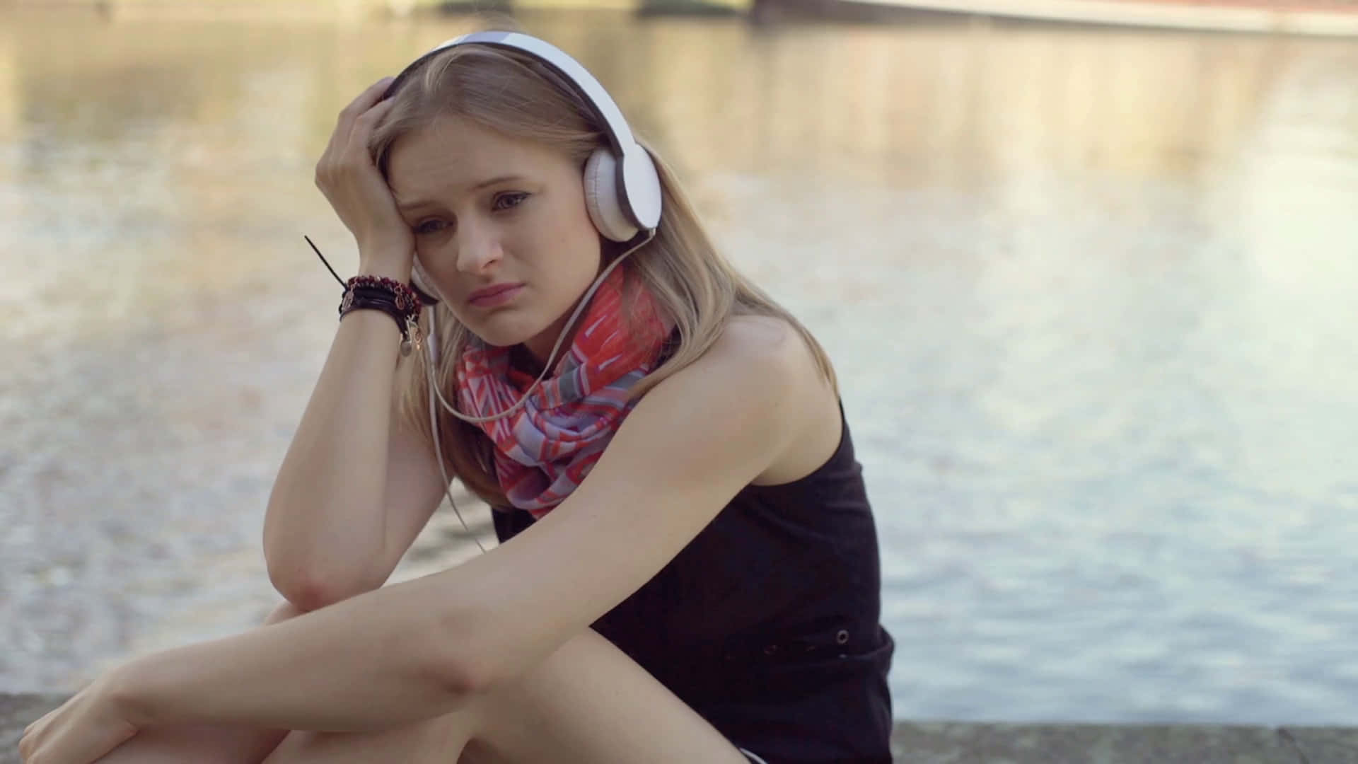 A Girl Sitting On The Edge Of A River With Headphones On