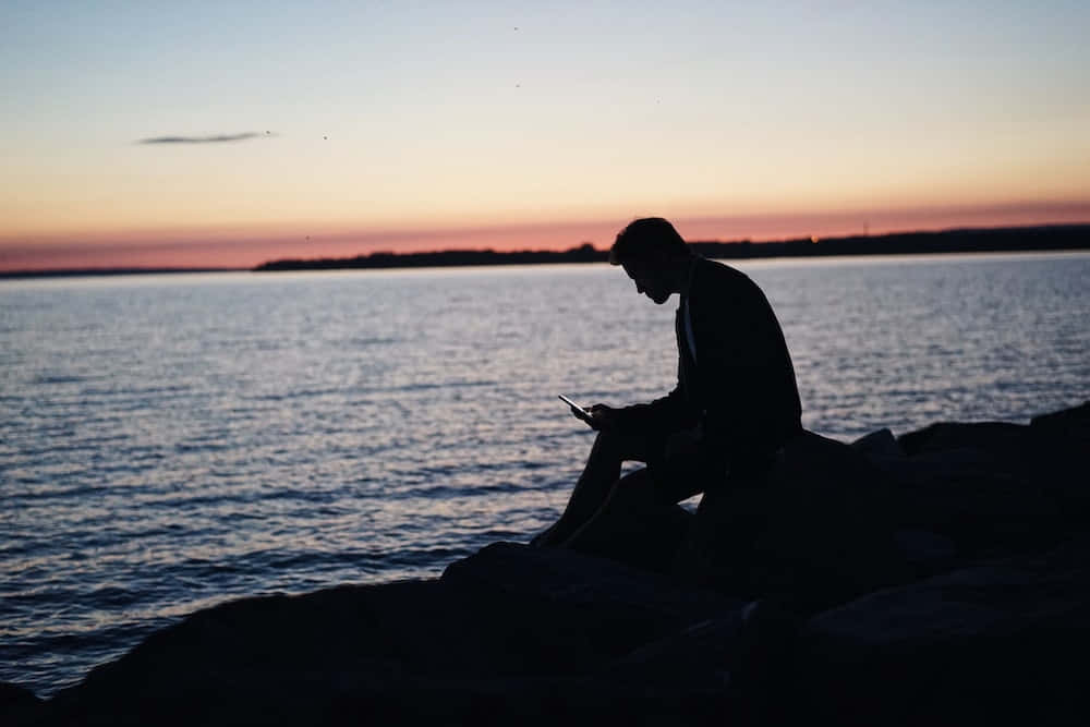 Man Sitting On Rocks At Sunset