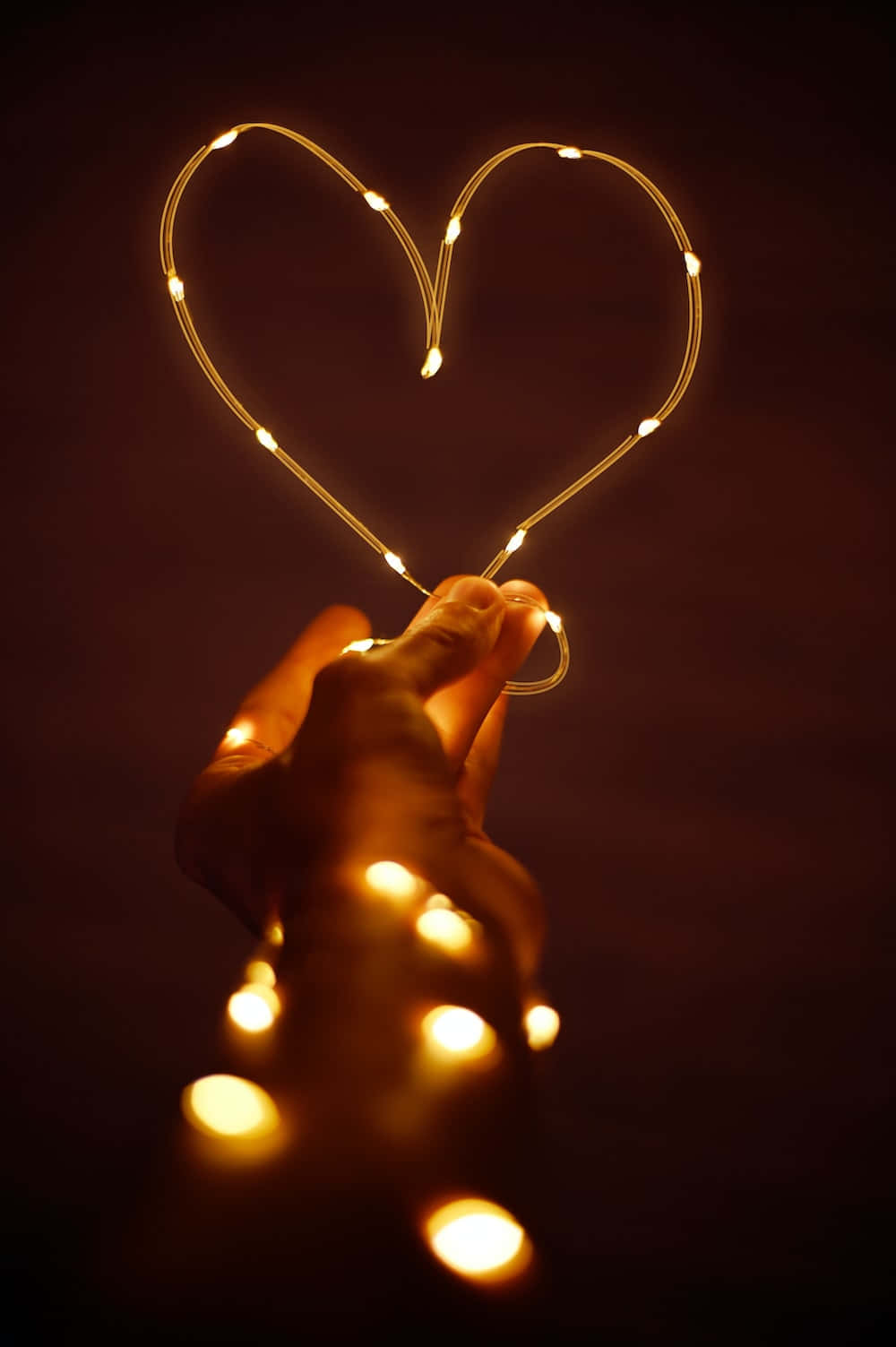 A Person Holding A Heart Shape With Lights In It