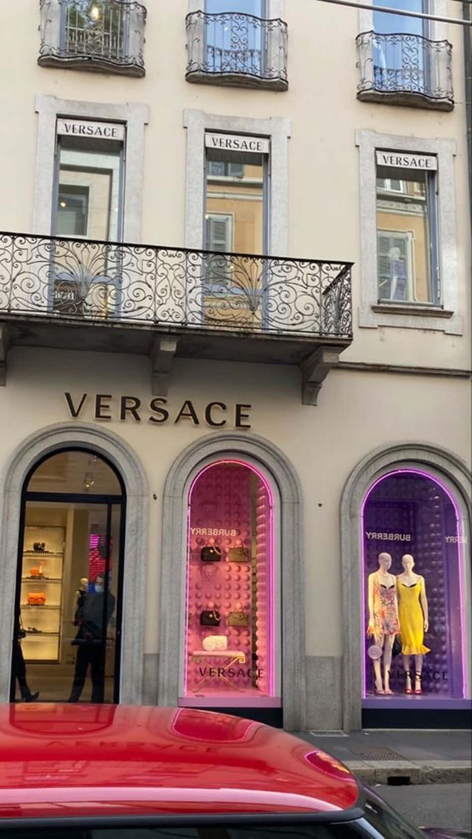 Versace - en butik med en rød bil foran Wallpaper