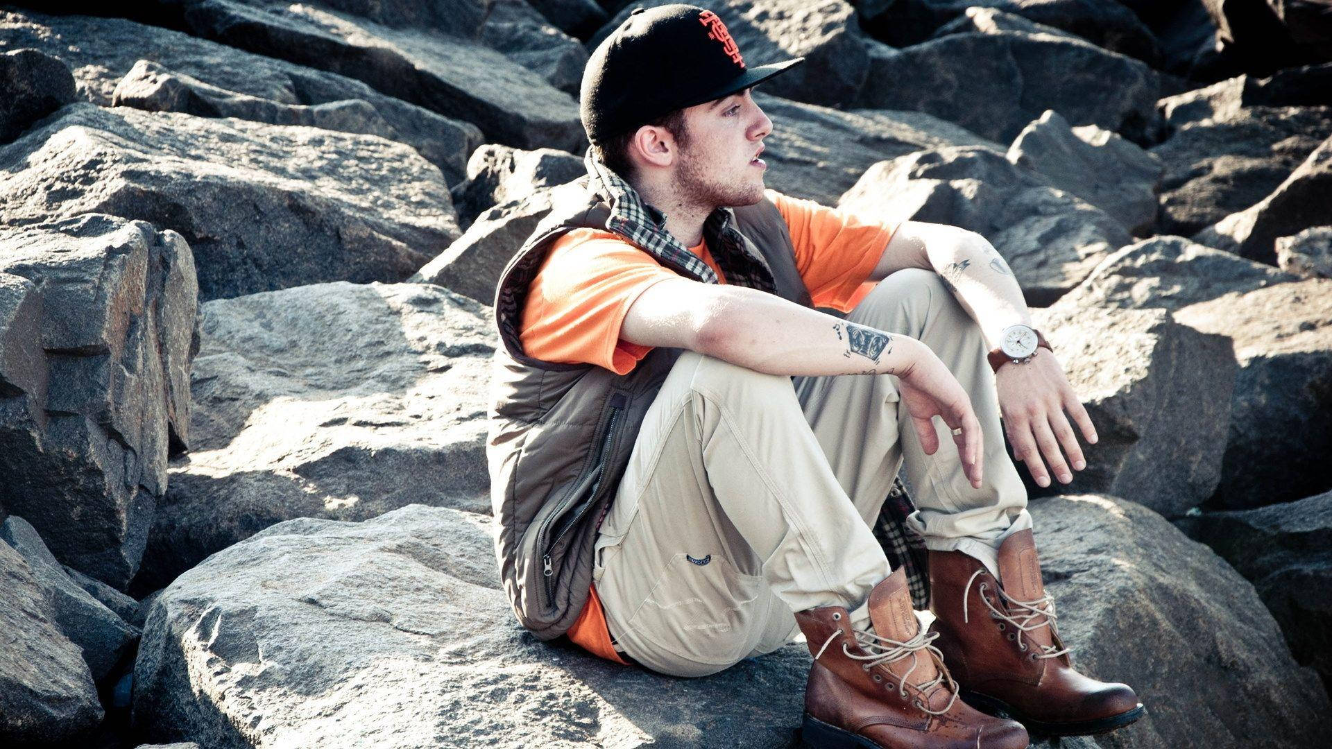 Mac Miller Sitting On Rocks Wallpaper