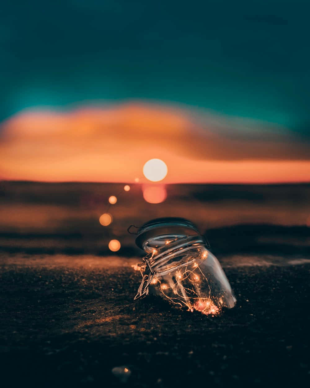 a glass jar sitting on the beach at sunset