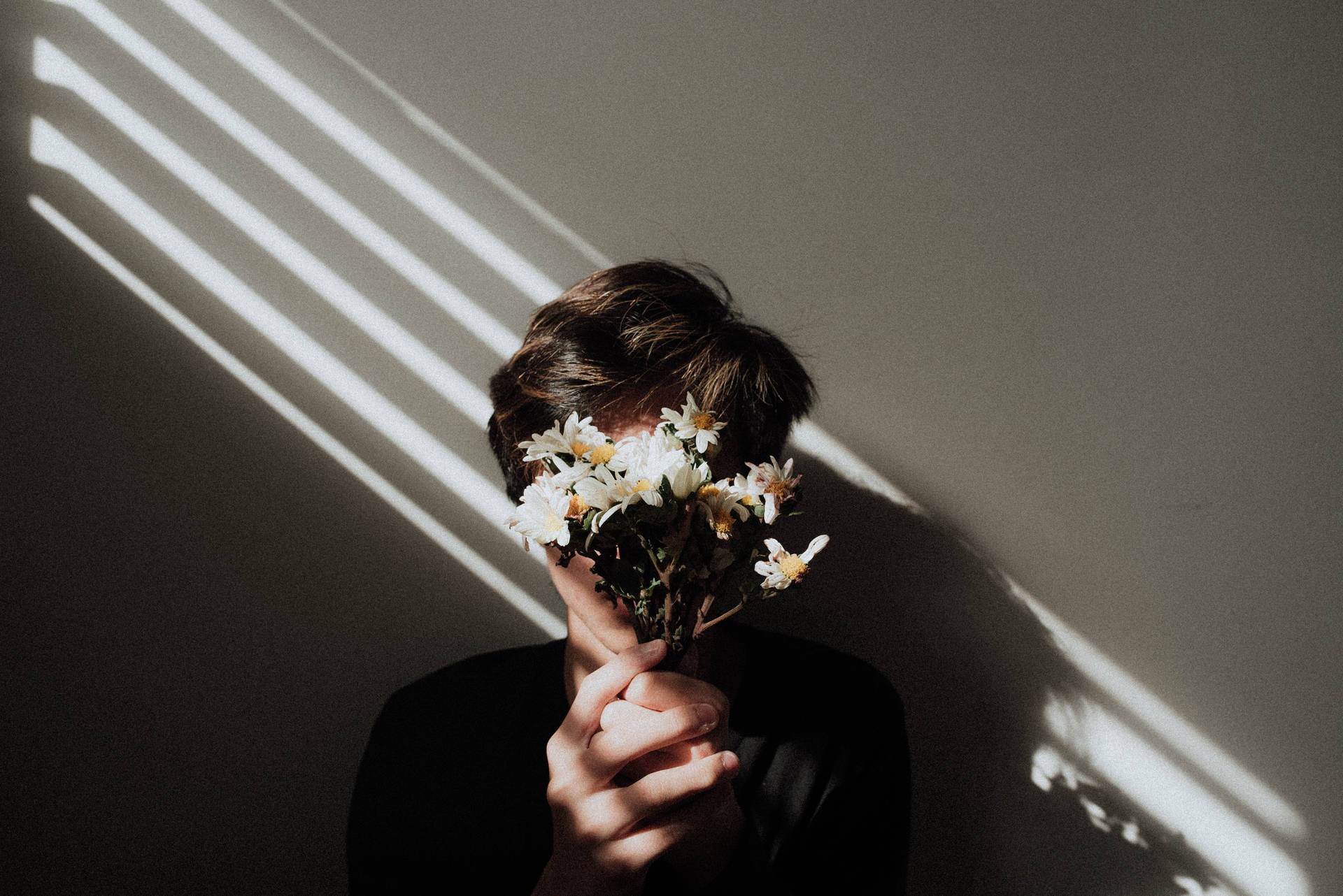 Aesthetic wallpaper of a photography of a man holding daisy flowers over his face. 