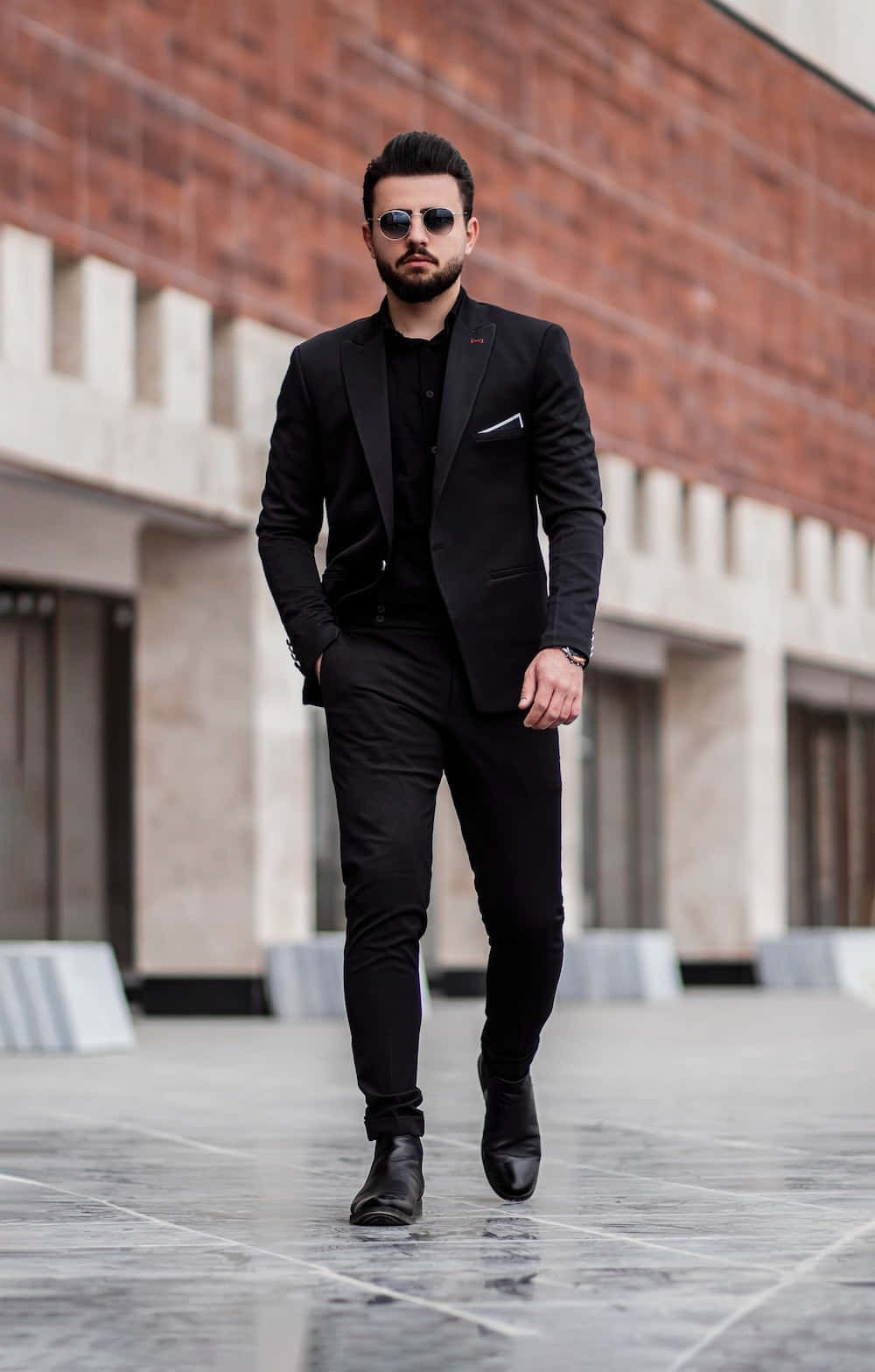 A Man In A Black Suit Walking Down A Street