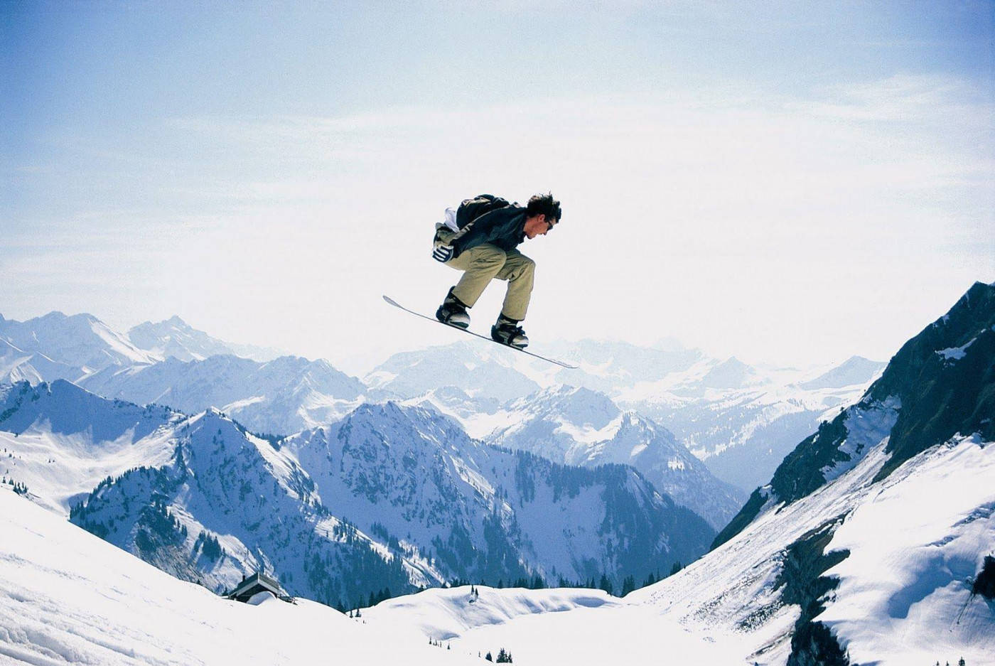 Man With Snowboard Descending With Mountainous Backdrop Background