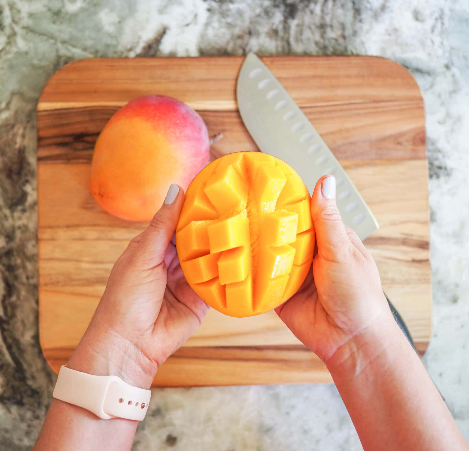 A Woman's Hand Holding A Mango On A Cutting Board