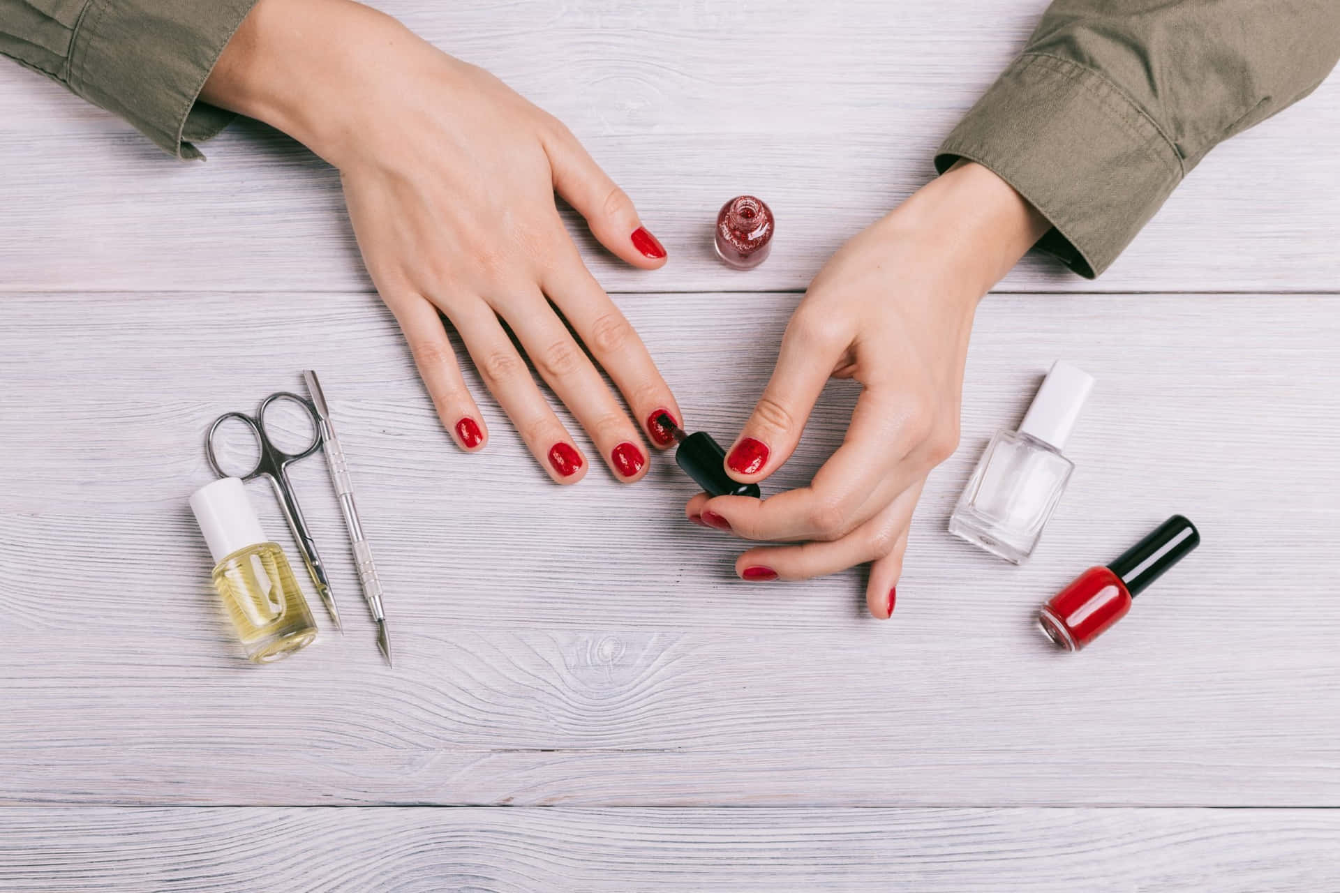 A Woman's Hands With Red Nail Polish And Other Tools On A Wooden Table