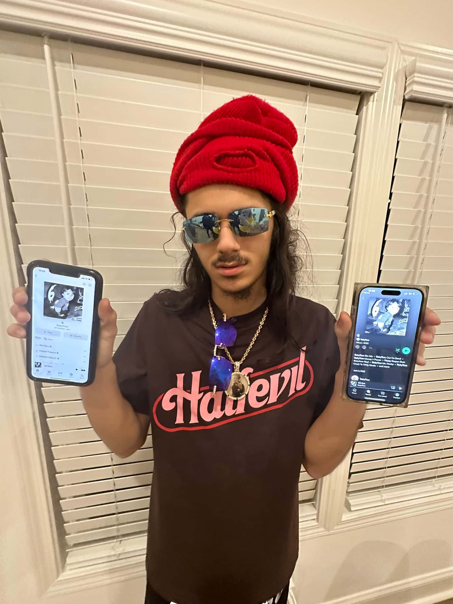 Manwith Red Beanieand Sunglasses Holding Two Phones Wallpaper