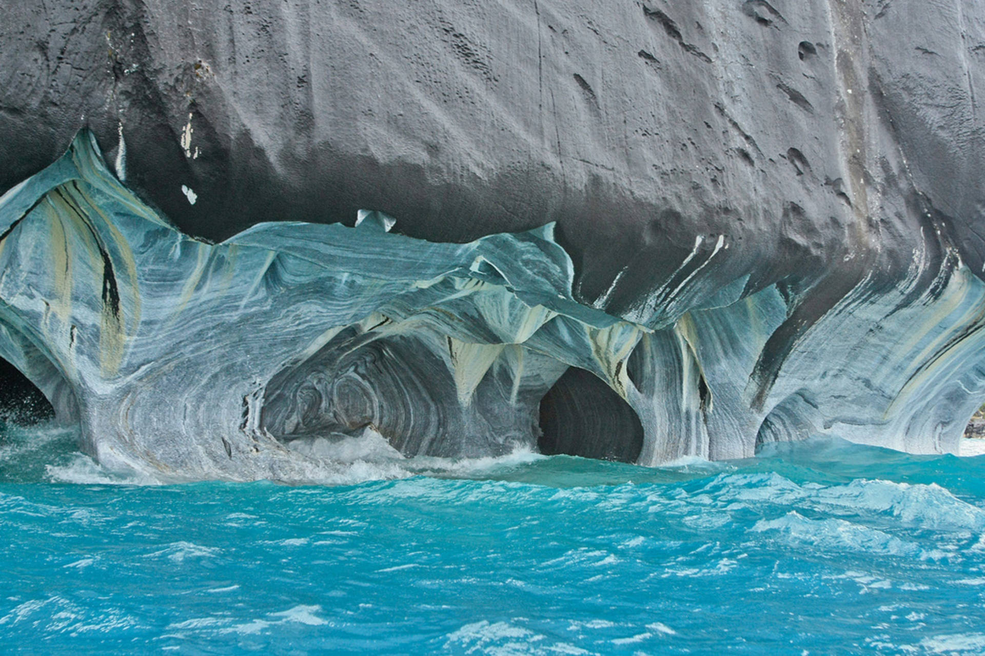 Visitors admire the stunning blue and gold marble formations of Marble Caves, Chile Wallpaper