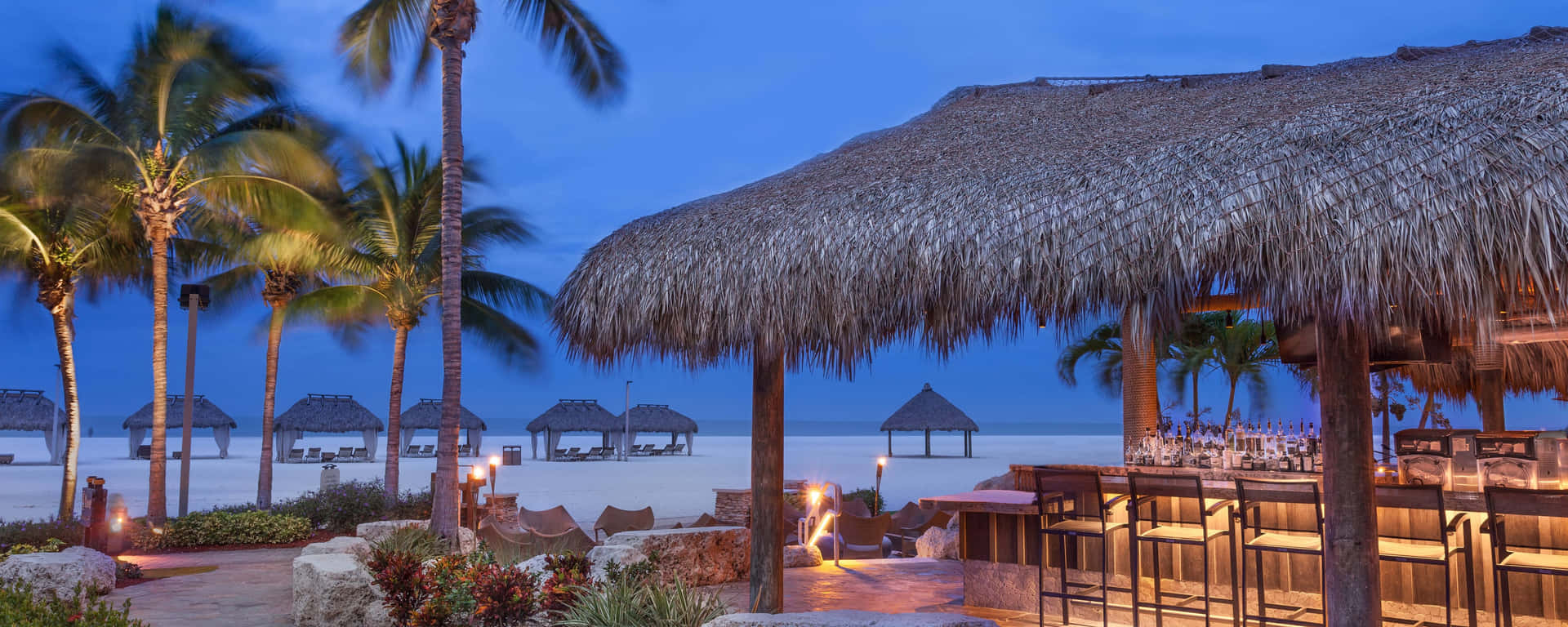 A Beach Bar With Thatched Roofs And Palm Trees