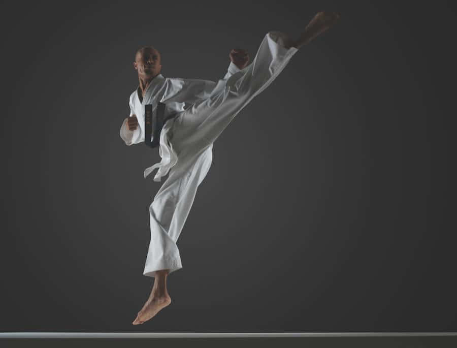 Young martial artist striking a high kick pose in a white training uniform Wallpaper