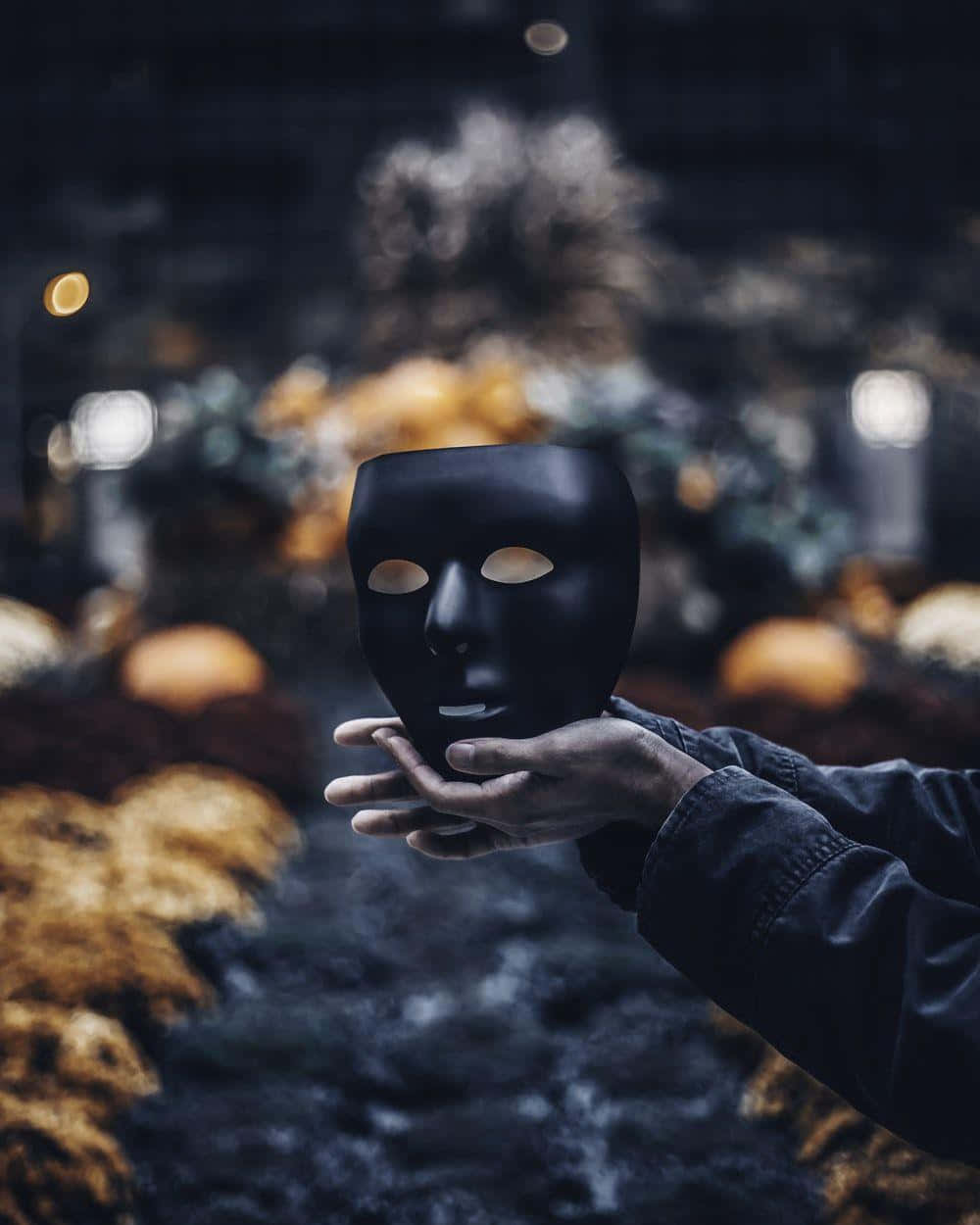 A Person Holding A Black Mask In Front Of A Pumpkin Patch