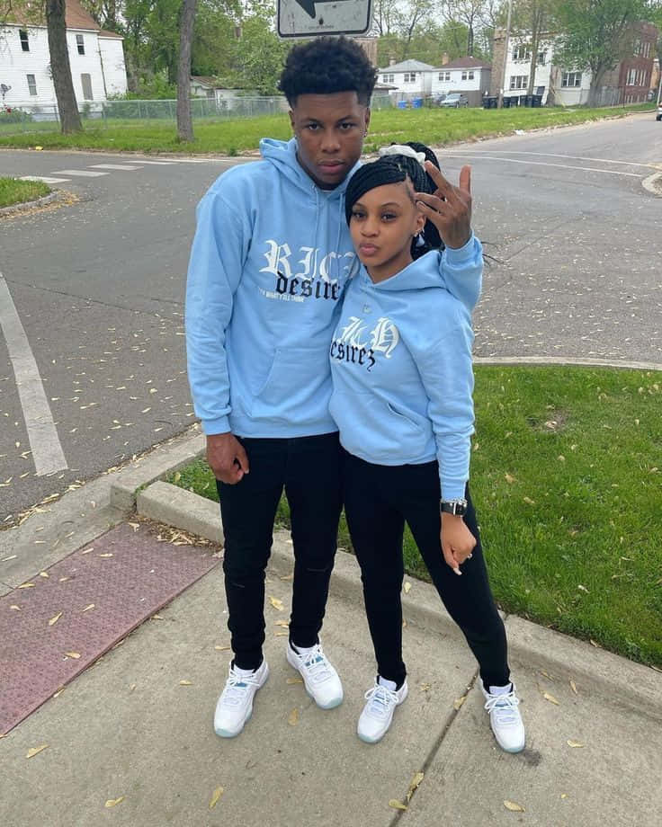 A Couple Standing On The Sidewalk Wearing Blue Hoodies