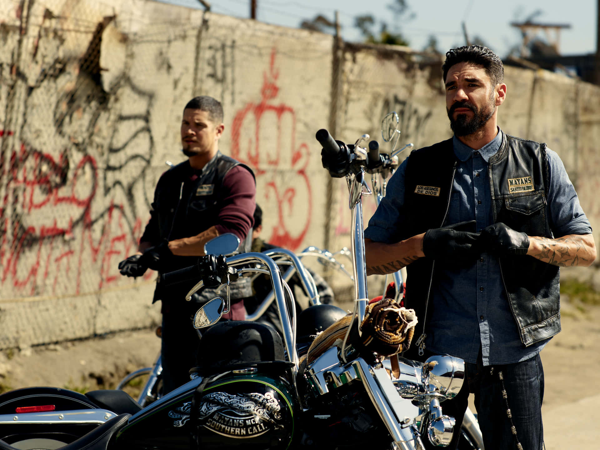 To mænd står ved siden af motorcykler foran en mur af klipper. Wallpaper