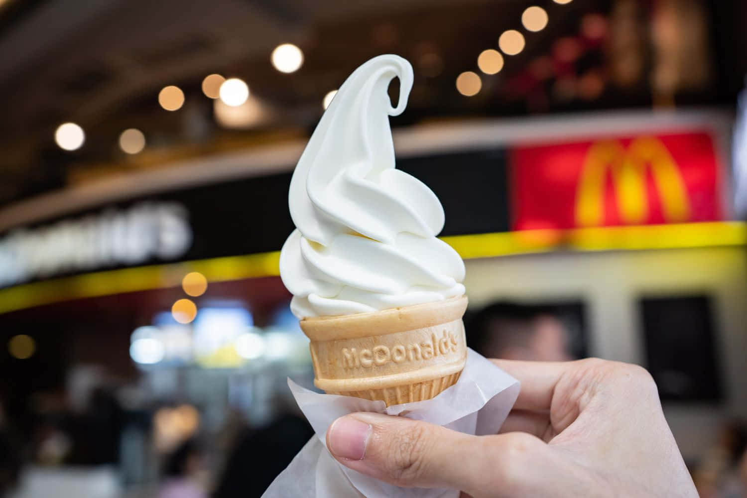 A Person Holding An Ice Cream Cone In Front Of A Mcdonald's