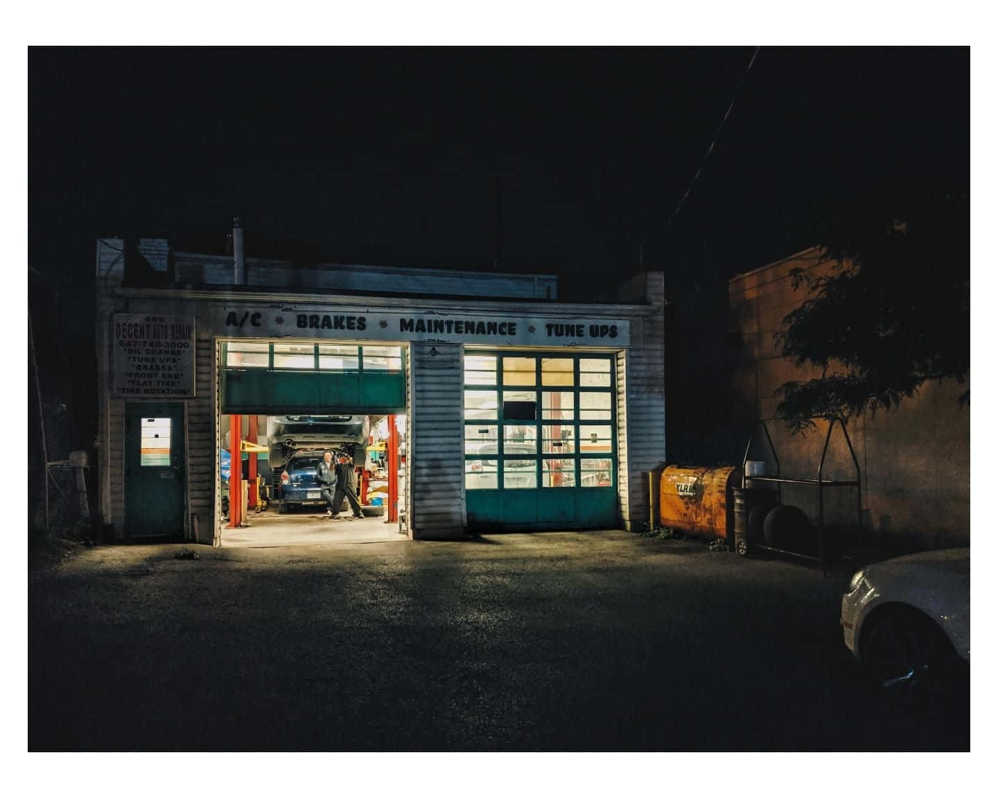A Garage At Night With Cars Parked In Front Of It