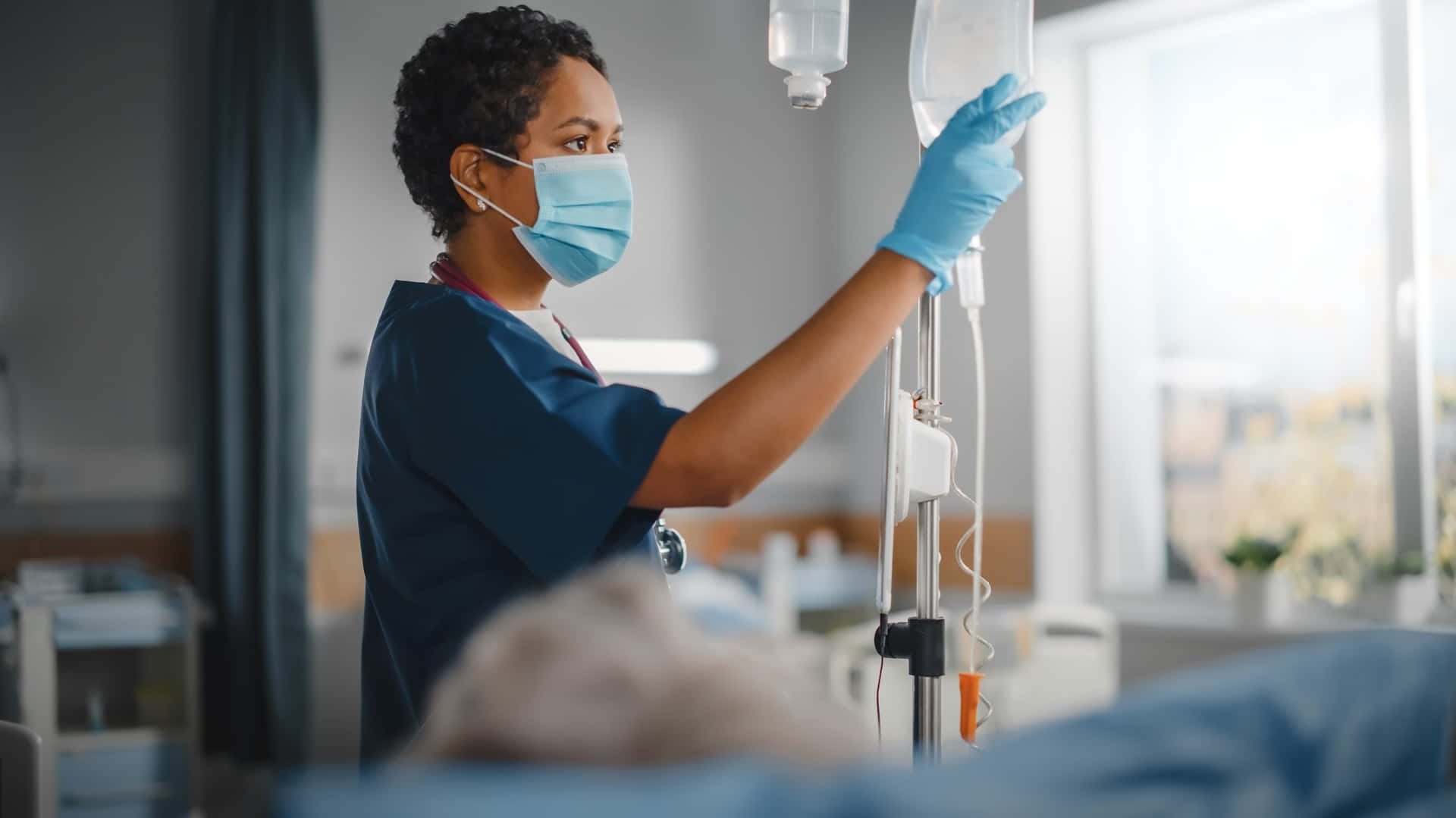 A Nurse Is Holding An Iv Bag In A Hospital Room