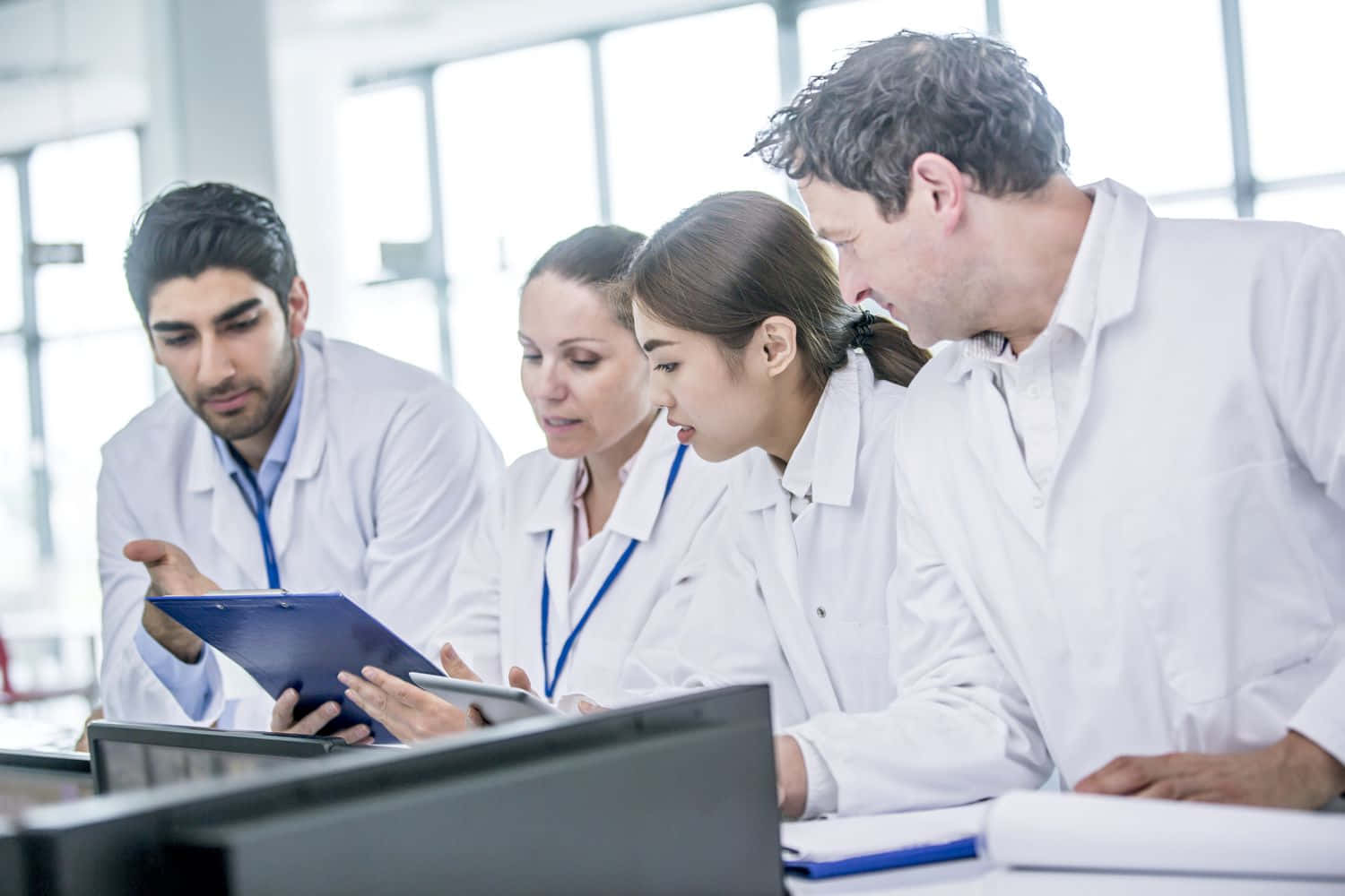 A Group Of People In Lab Coats Looking At A Tablet