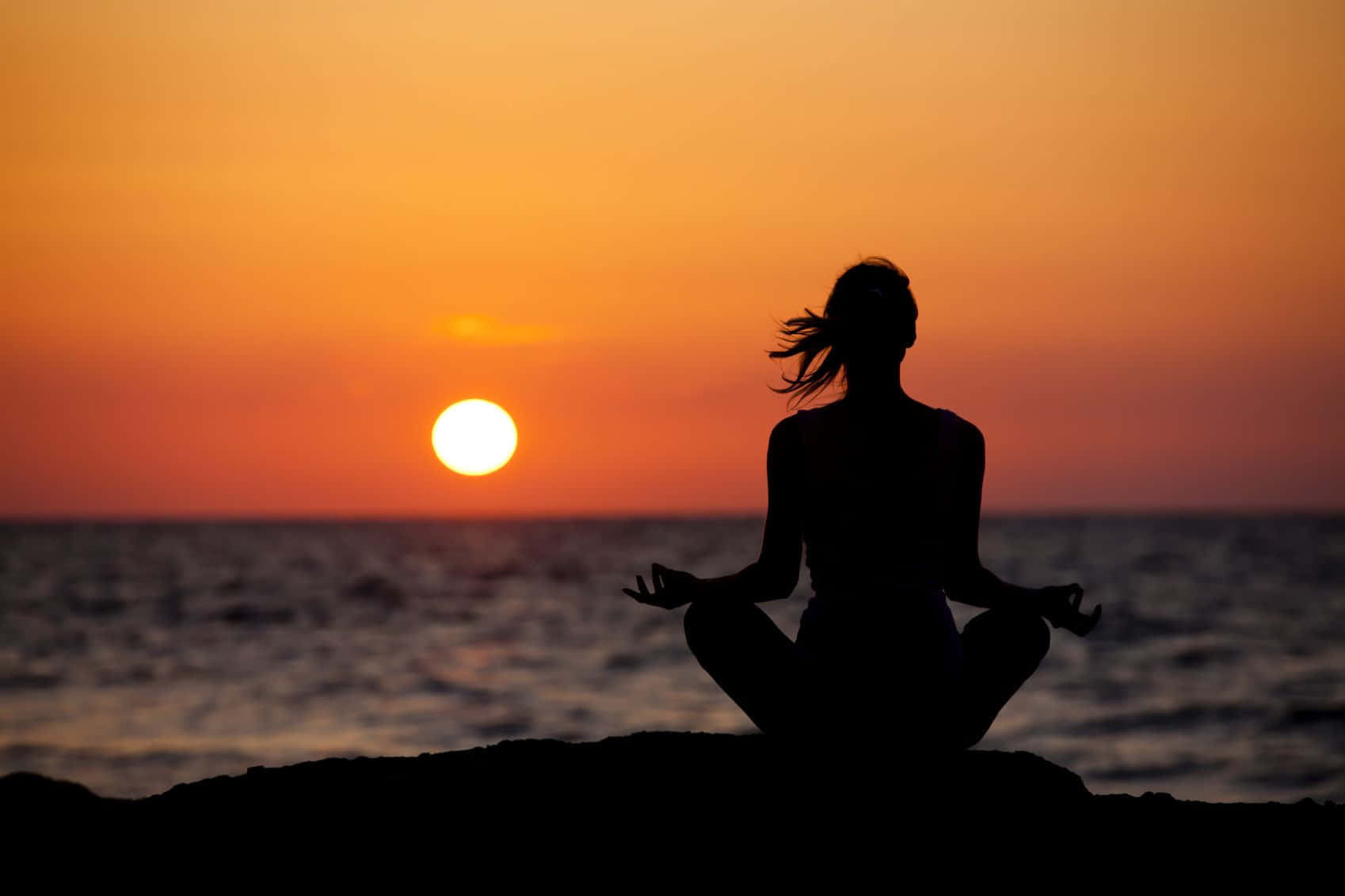 A Woman Is Meditating On The Beach At Sunset