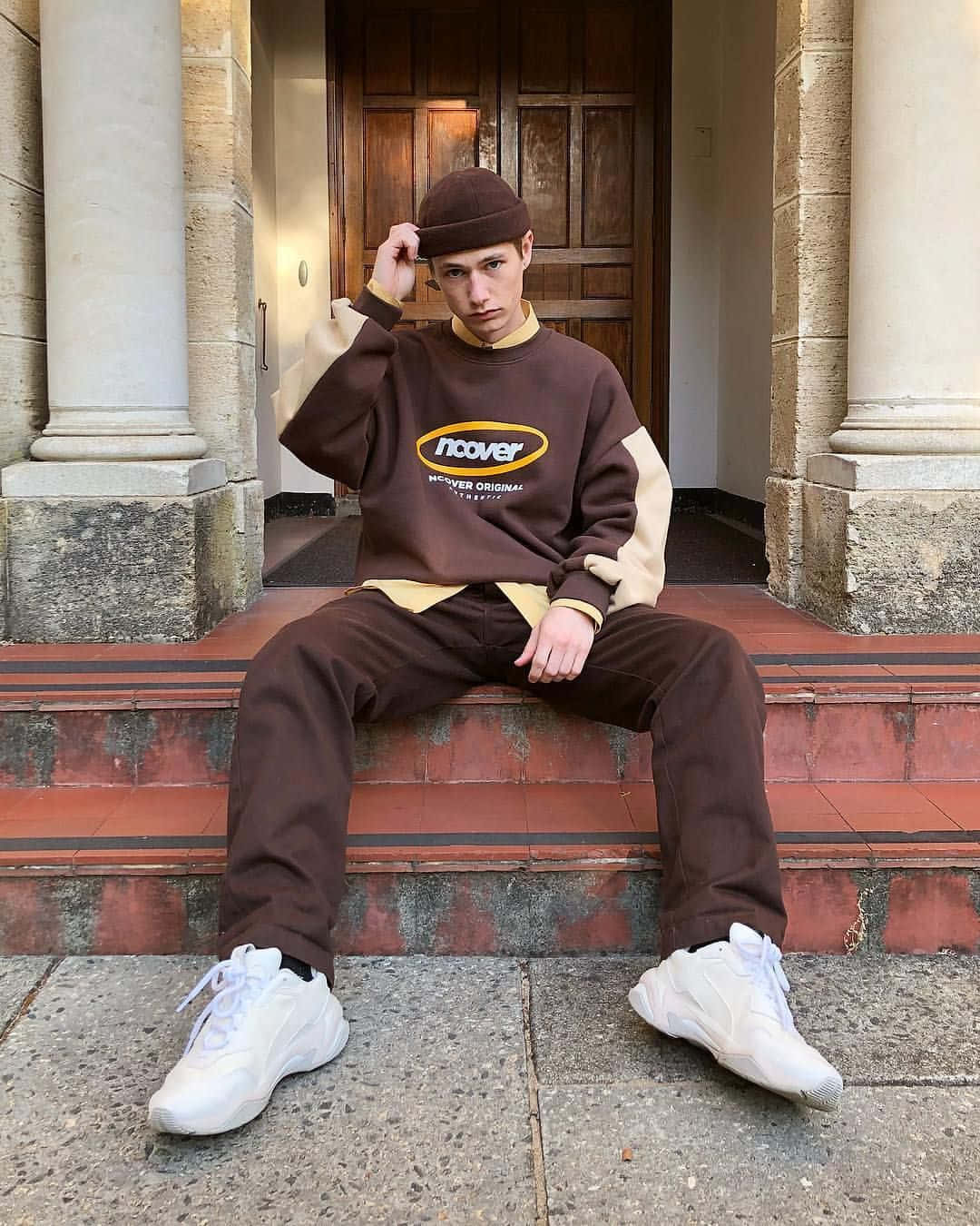 A Man Sitting On Steps Wearing A Brown Sweatshirt And Hat