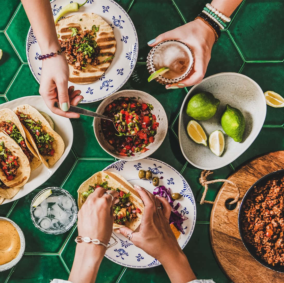A Group Of People Eating Tacos On A Green Tiled Table