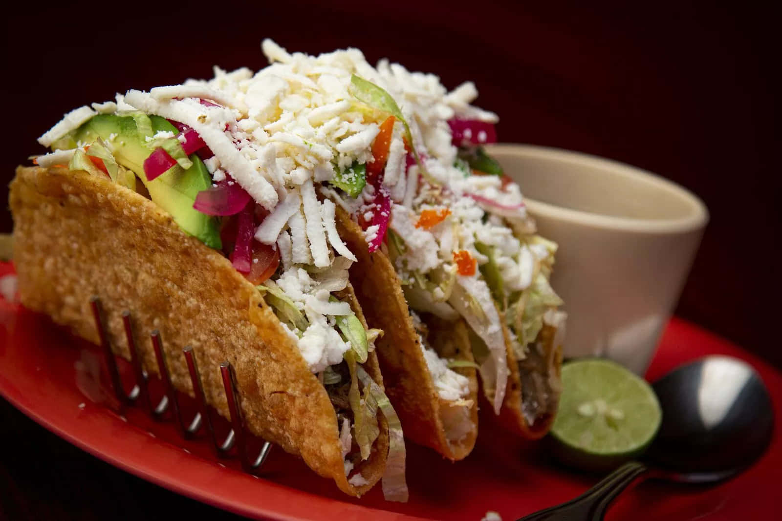 A Taco With Shredded Lettuce And Avocado On A Red Plate