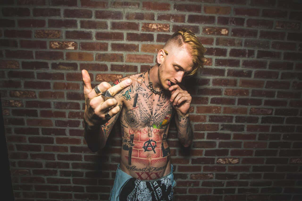 A Man With Tattoos Standing In Front Of A Brick Wall Wallpaper