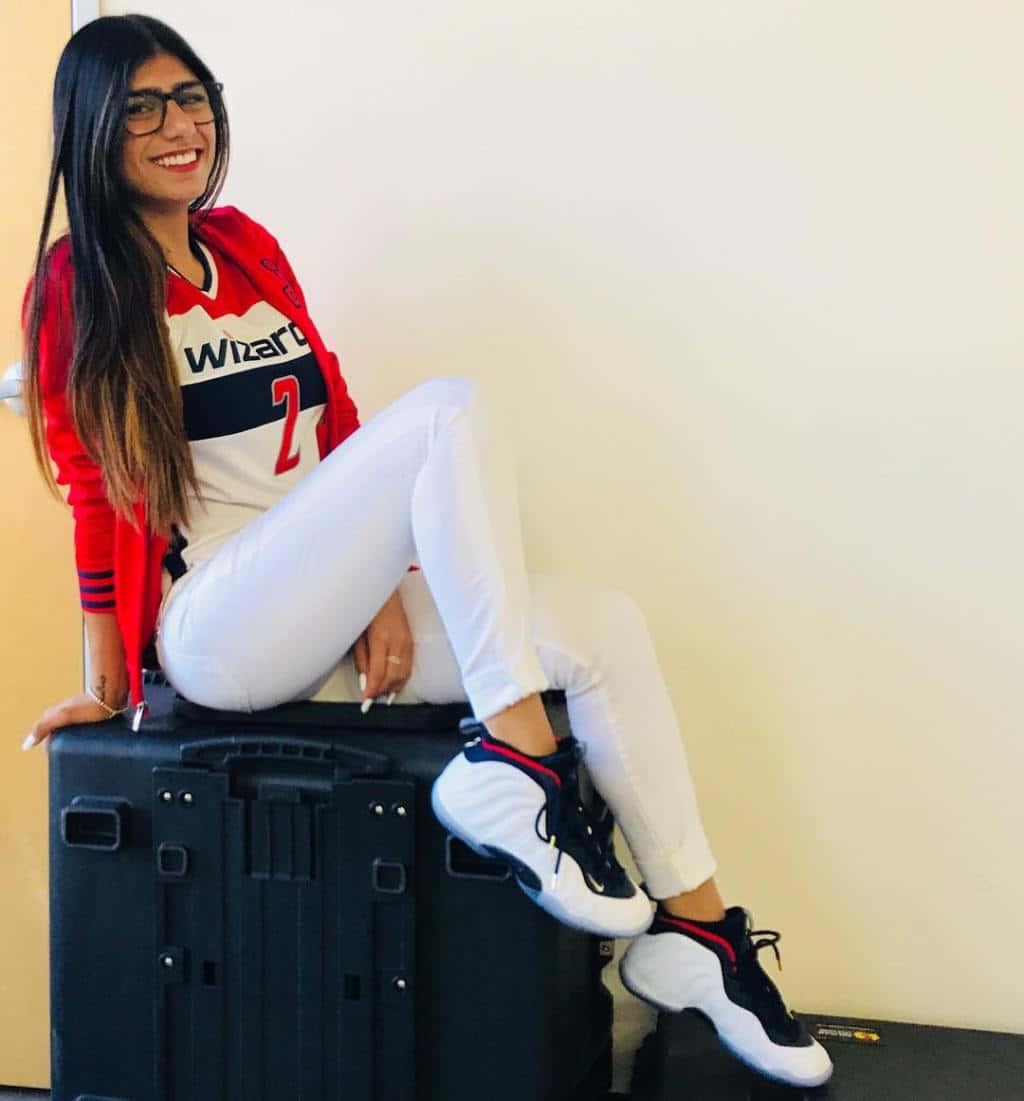 A Woman Sitting On A Suitcase With Sneakers