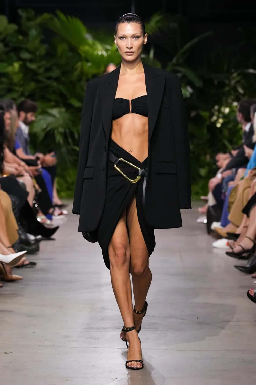 A Model Walks Down The Runway Wearing A Black Blazer And Skirt