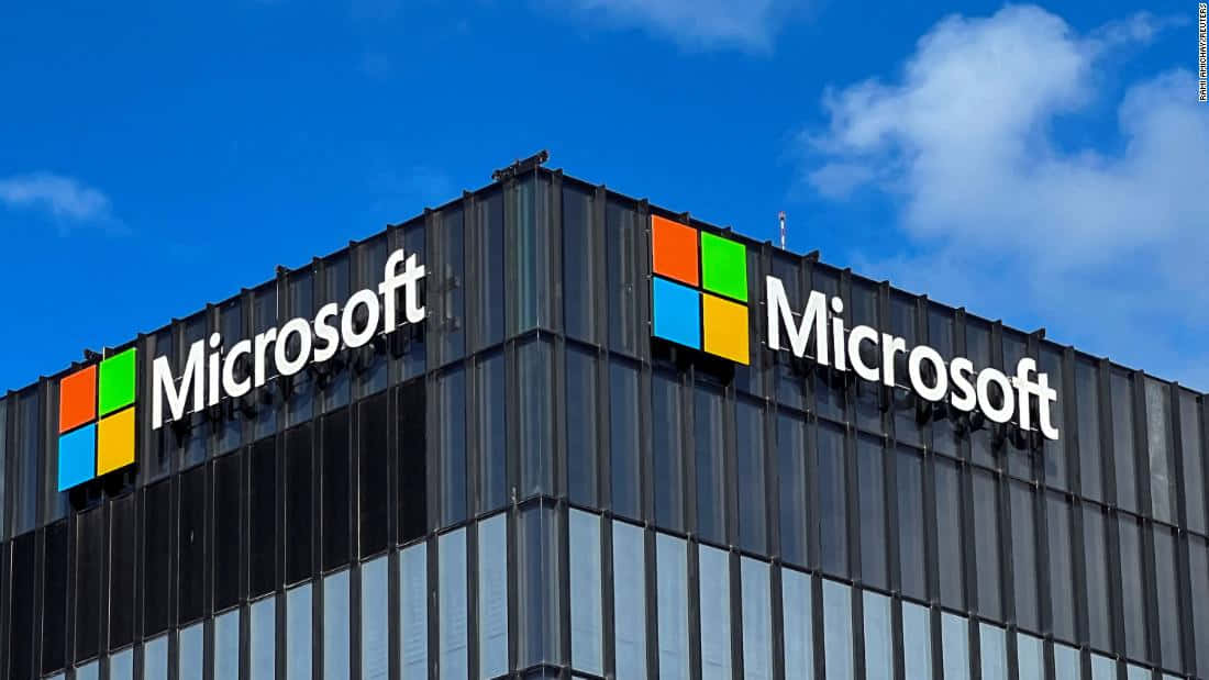 Microsoft is leading the way in innovation Picture — Microsoft logo in vibrant colors adorns a modern glass skyscraper against a bright blue sky with fluffy white clouds.