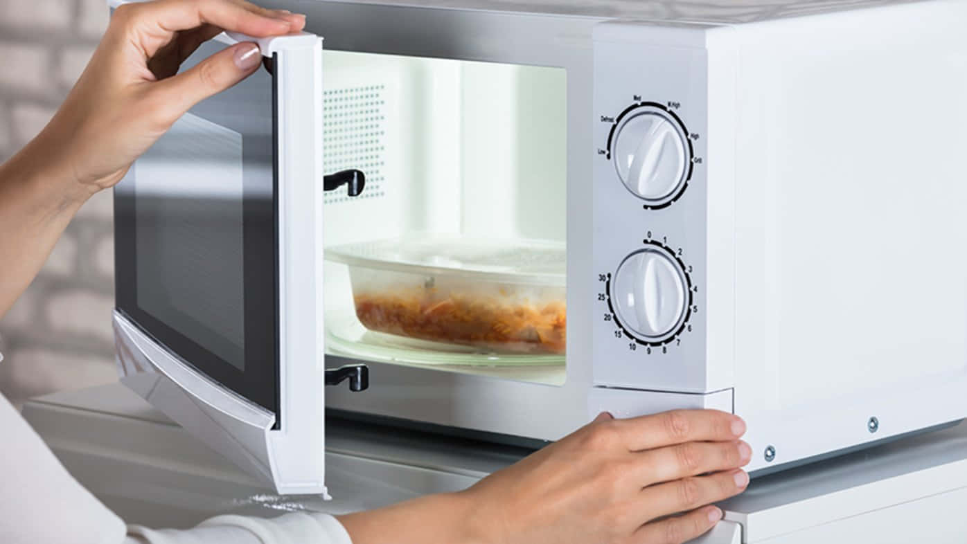 A Woman Is Opening The Door Of A Microwave
