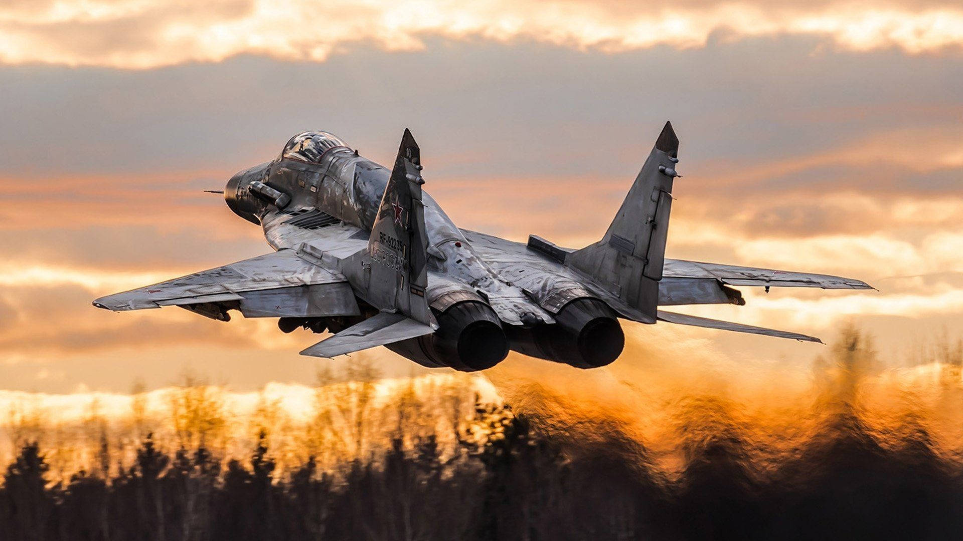 Caption: Majestic Mikoyan MiG-35 Fighter Jets Soaring Over a Forest Wallpaper