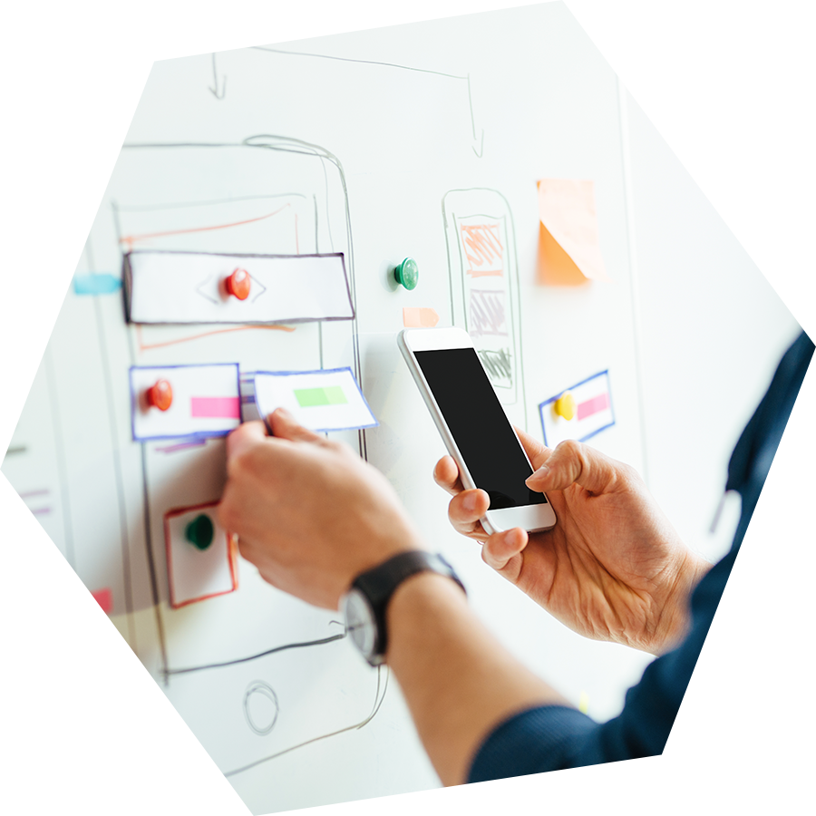 Mobile App Development Planning Session PNG — A person designs a mobile app interface on a whiteboard using physical cards and a smartphone for reference.