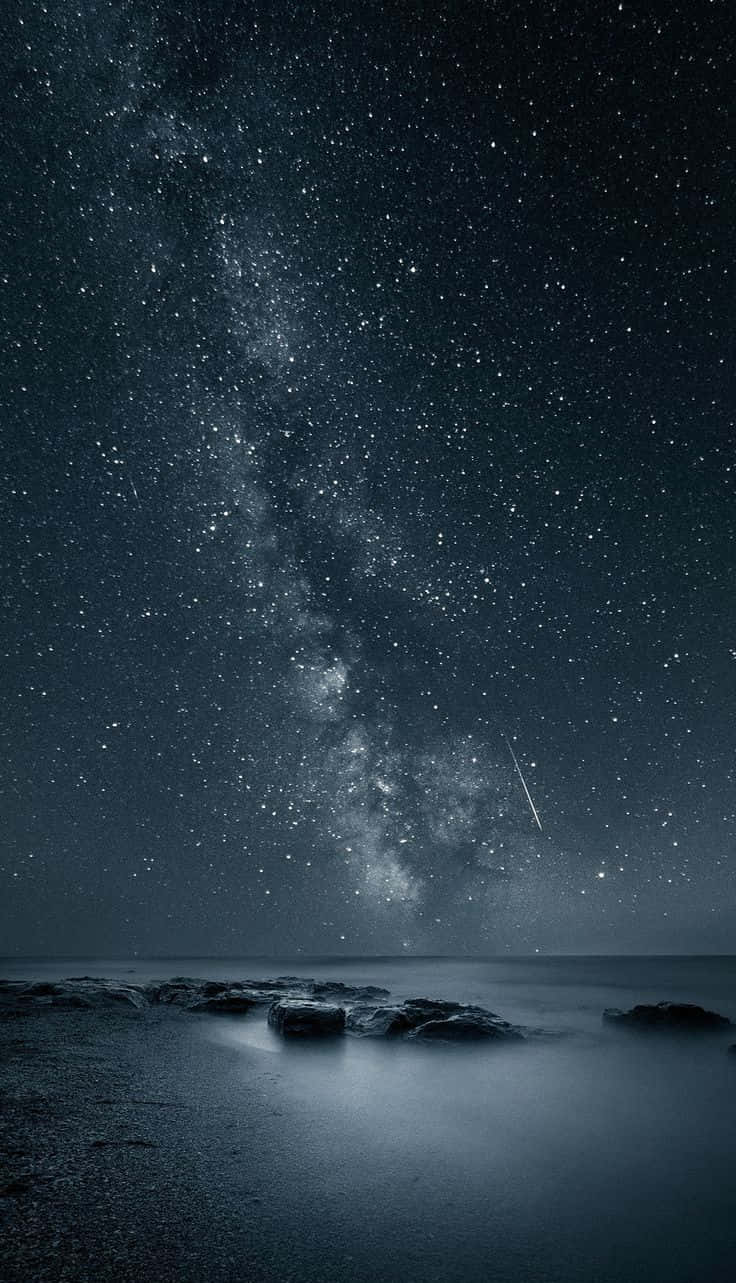 A Starry Sky Over A Beach With Rocks And Milky