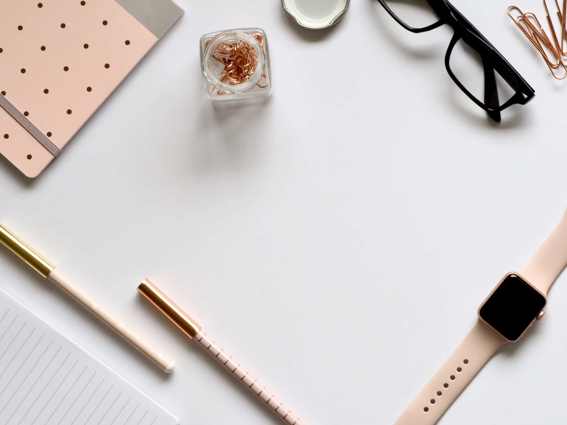 A White Table With A Pink Apple Watch, Glasses, And A Notebook